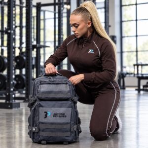 Beyond Peptides Gym Backpack standing open on a gym floor next to a kneeling athlete