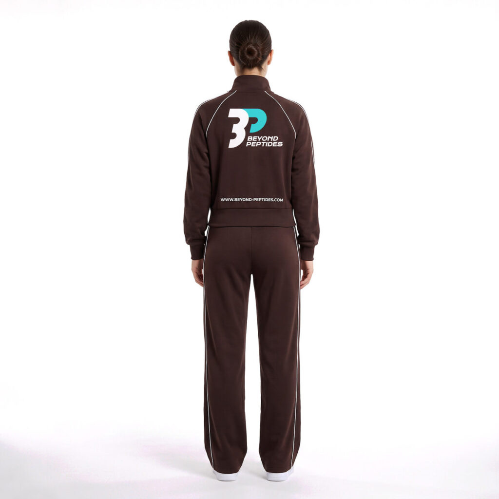 Model wearing the Beyond Peptides Women's Tracksuit Set in dark brown, relaxed fit with wide-leg trousers, back view showing the large logo across the back. AI-generated image, actual product may differ.