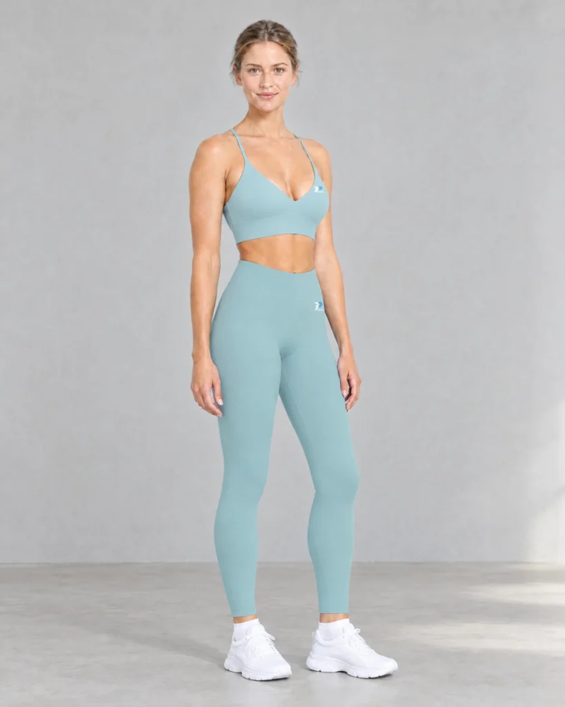 Model in the arctic blue Women's Leggings and Sports Bra standing in a light concrete studio